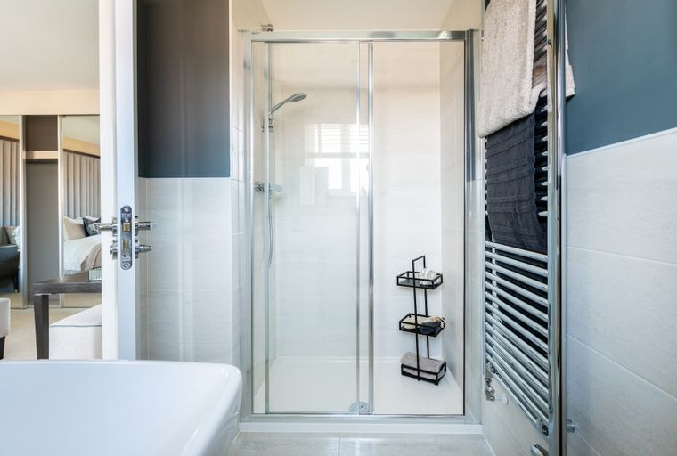 A bathroom with a glass shower enclosure, a towel warmer, and a shelving unit.