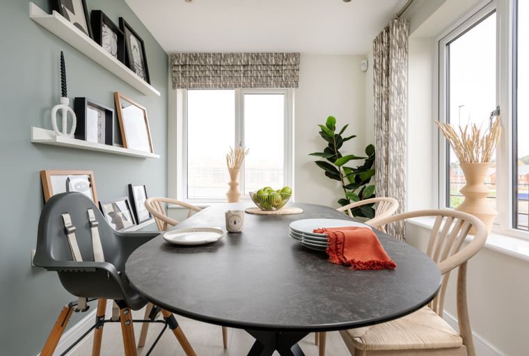 A dining table with chairs and a high chair in a room with shelves and windows.
