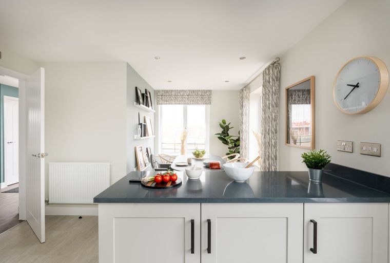 A kitchen island with a dark countertop and white cabinets, featuring tomatoes on a cutting board and a bowl.