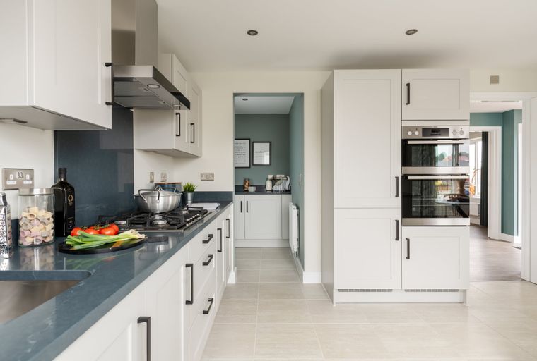 A modern kitchen with white cabinets, a dark countertop, a gas stovetop, and a double oven.