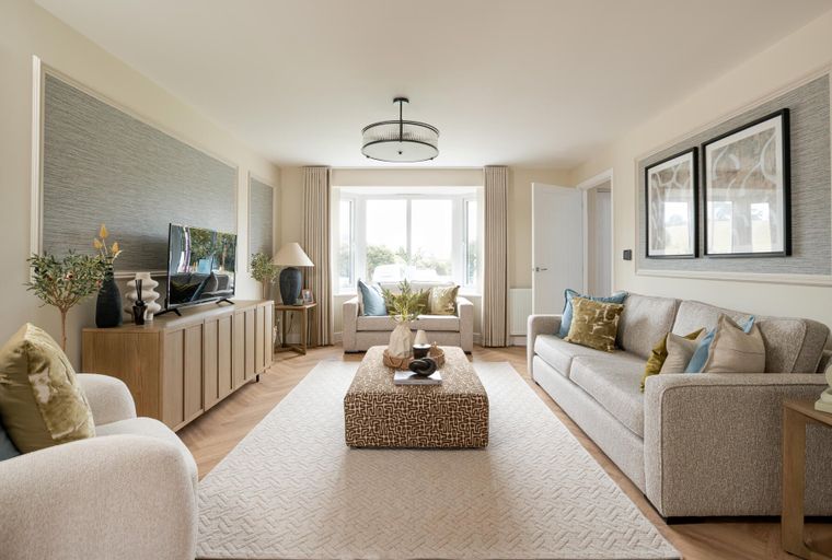 A living room with sofas, an ottoman, a television, and a bay window.