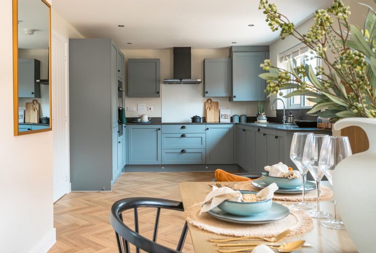 A kitchen with blue-grey cabinets, a black extractor hood, and a dining table set for a meal.