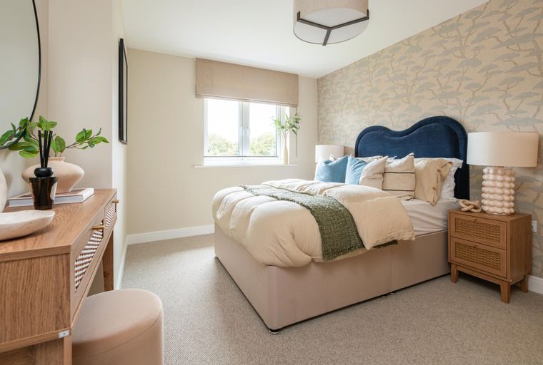 A bedroom with a bed, nightstand, vanity, and a window.