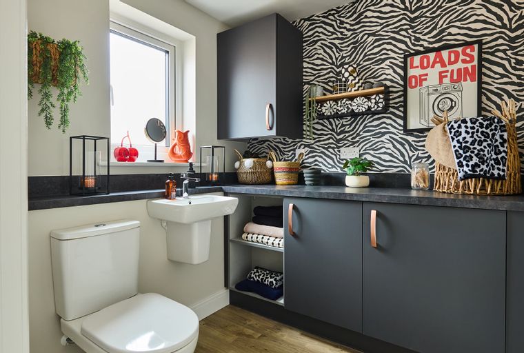A laundry room with a toilet, sink, cabinets, and zebra print wallpaper.