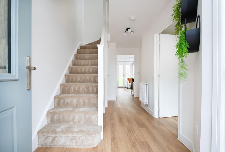 A hallway with a carpeted staircase, wood-look flooring, and a doorway leading to a living area.