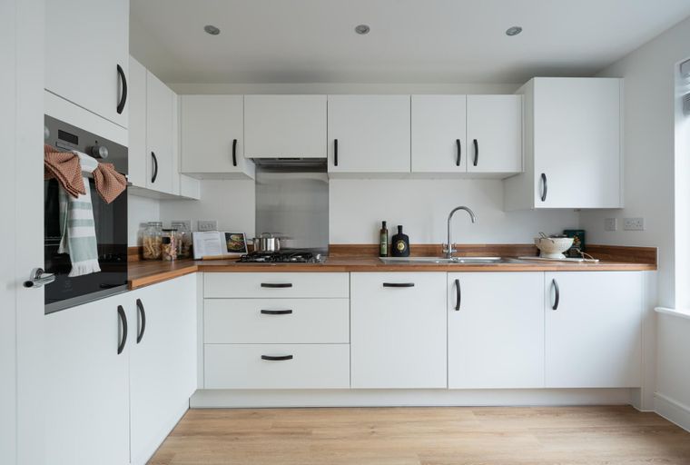 A modern kitchen with white cabinets, wooden countertops, and a stainless steel backsplash.