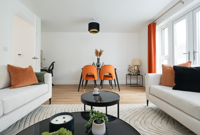 A living and dining room with white sofas, orange chairs, and a dining table.