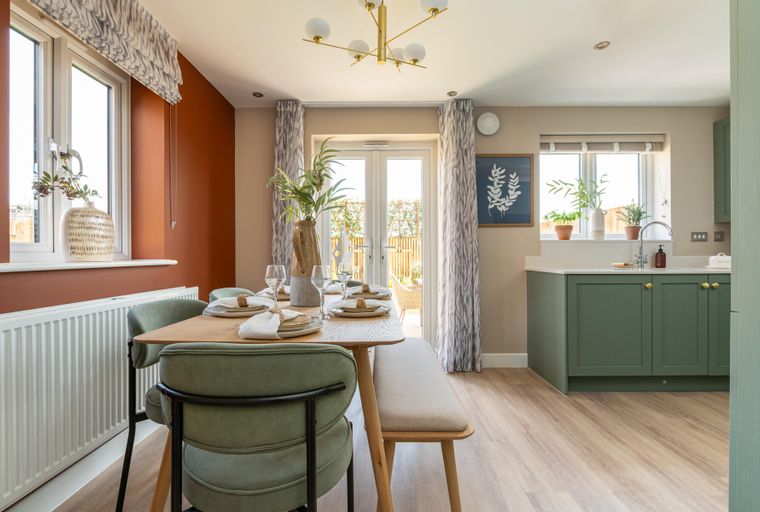 A dining area with a wooden table, chairs, and a bench, adjacent to a kitchen with green cabinets.