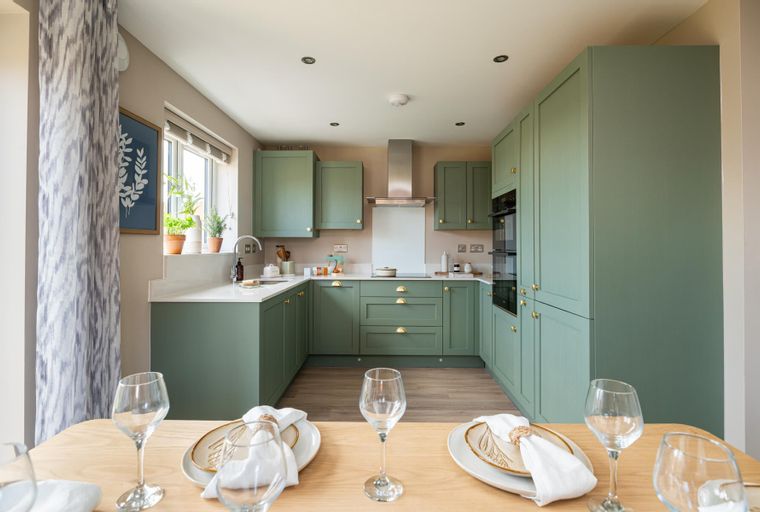 A kitchen with sage green cabinets, white countertops, and a stainless steel range hood.