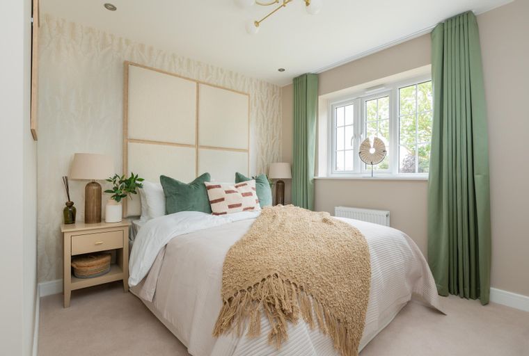A bedroom with a bed, pillows, a throw blanket, a bedside table, and a window with curtains.