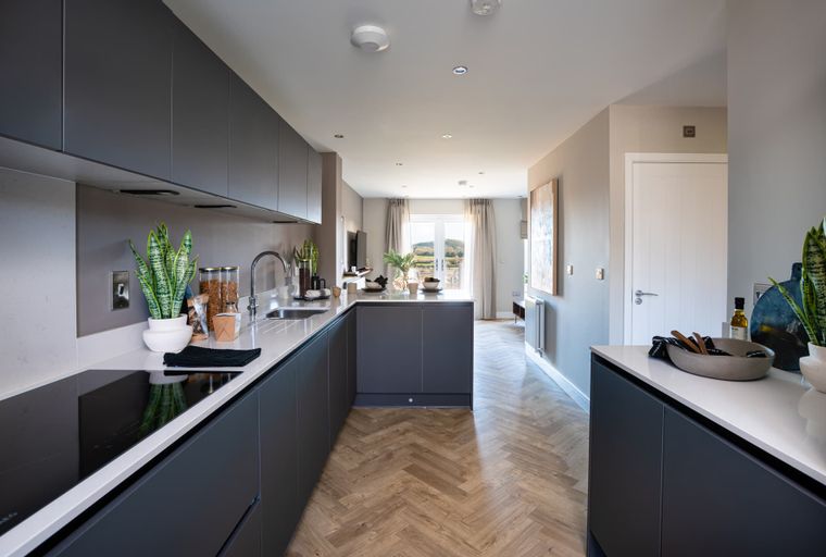 A modern kitchen with dark cabinets, a kitchen island, and herringbone wood flooring.