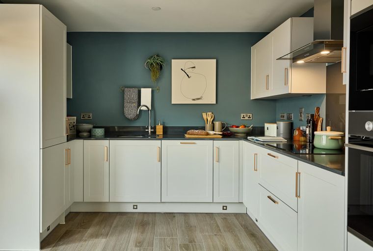 A modern kitchen with white cabinets, a teal accent wall, and a dark countertop.