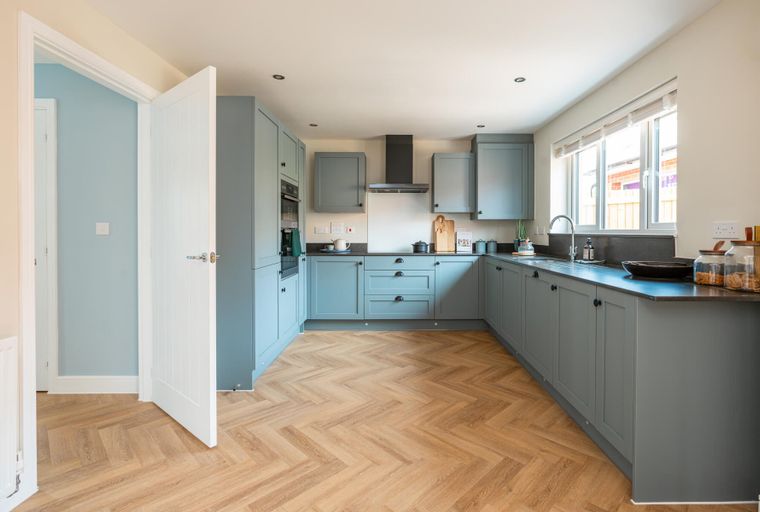 A modern kitchen with blue-grey cabinets, dark countertops, and herringbone flooring.