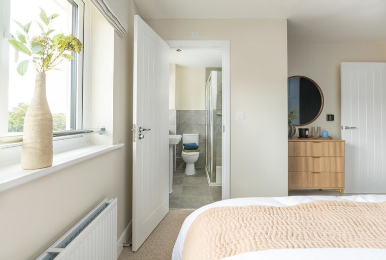 A bedroom with a bed, a vase, a dresser, a mirror, and an open door to a bathroom.