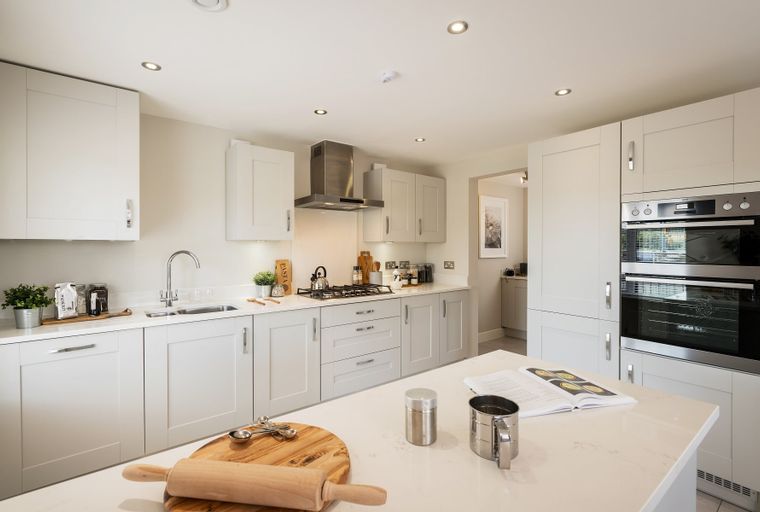 A modern kitchen with light gray cabinets, a quartz island, and stainless steel appliances.