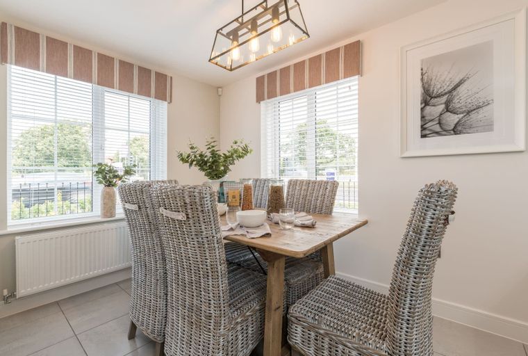 A dining room with a wooden table, wicker chairs, and windows.