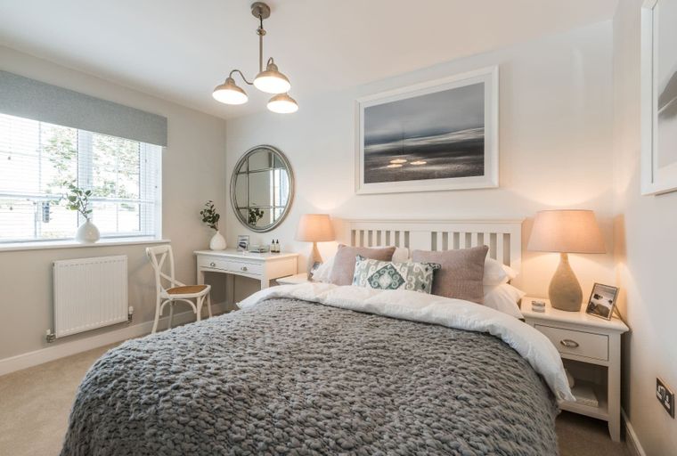 A bedroom with a bed, bedside tables, a vanity, and a window.