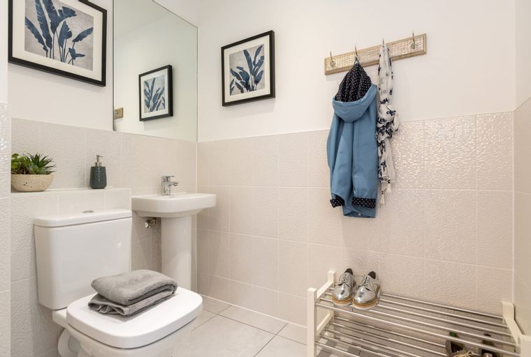 A bathroom with a toilet, sink, framed art, and a coat rack.