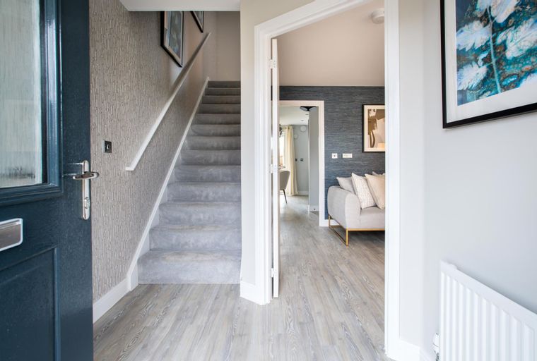 A hallway with a staircase and an open doorway to a living room.
