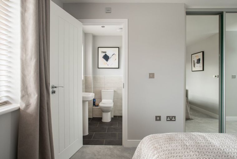 A bedroom with an open door revealing a bathroom with a toilet and sink, and a mirrored wardrobe.