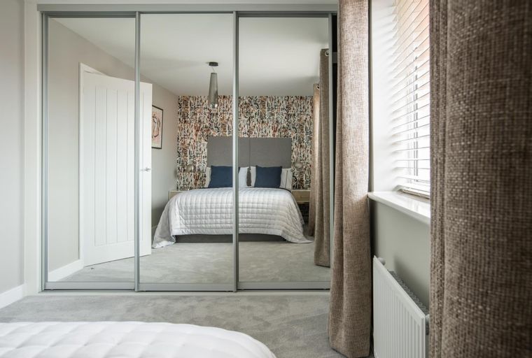 A bedroom with a bed, mirrored closet doors, and patterned wallpaper.
