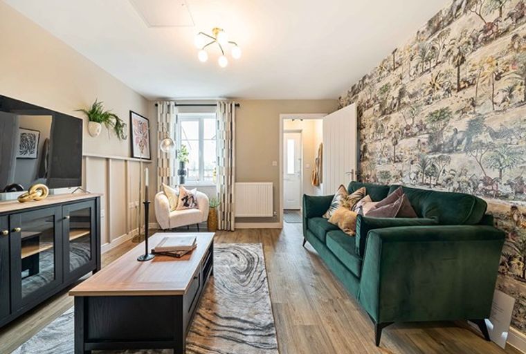 A living room with a green sofa, coffee table, and patterned wallpaper.