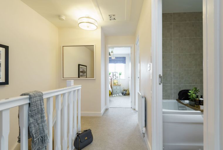 A hallway with a mirror, a balustrade, and an open doorway to a bathroom.
