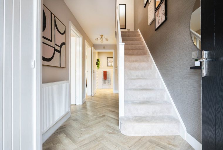 A hallway with a staircase, artwork, and herringbone flooring.