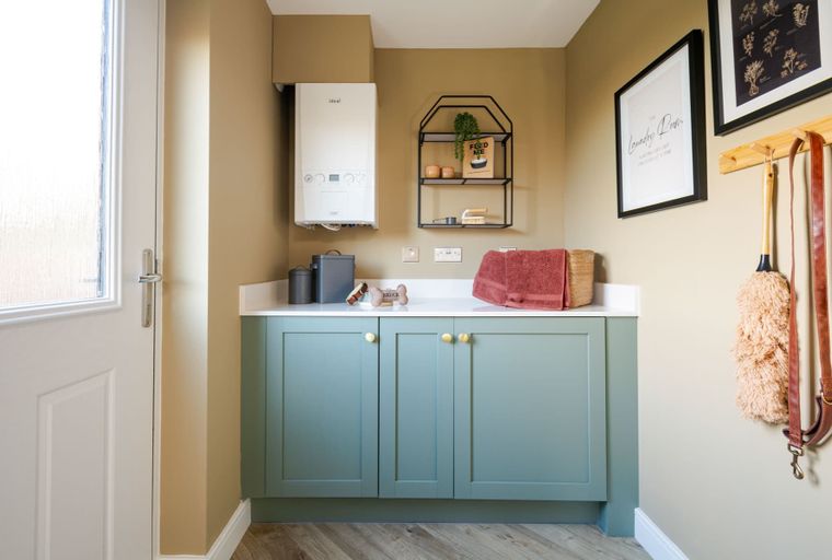 A utility room with a white boiler, sage green cabinets, and a white countertop.