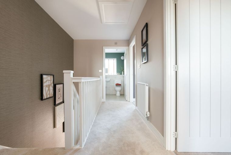 A hallway with a white railing and a door leading to a bathroom.
