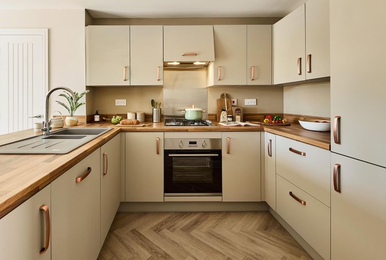 A kitchen with light-colored cabinets, copper handles, a sink, and an oven.
