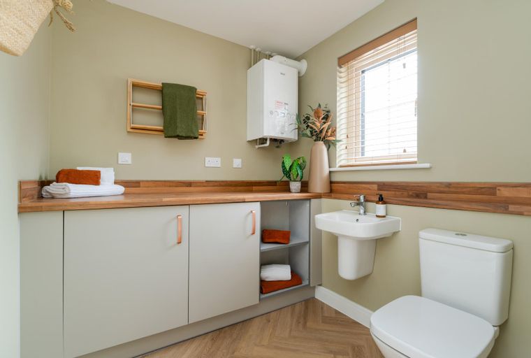 A utility room with a sink, toilet, cabinets, and a wall-mounted boiler.