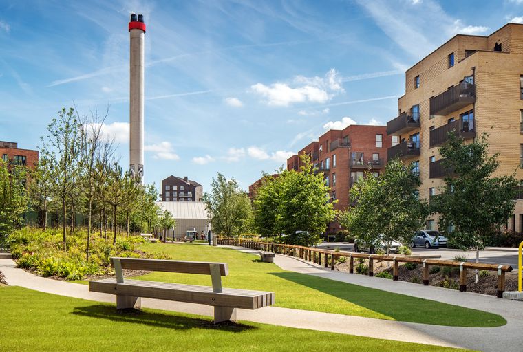 A park with modern apartment buildings and a tall chimney in the background.