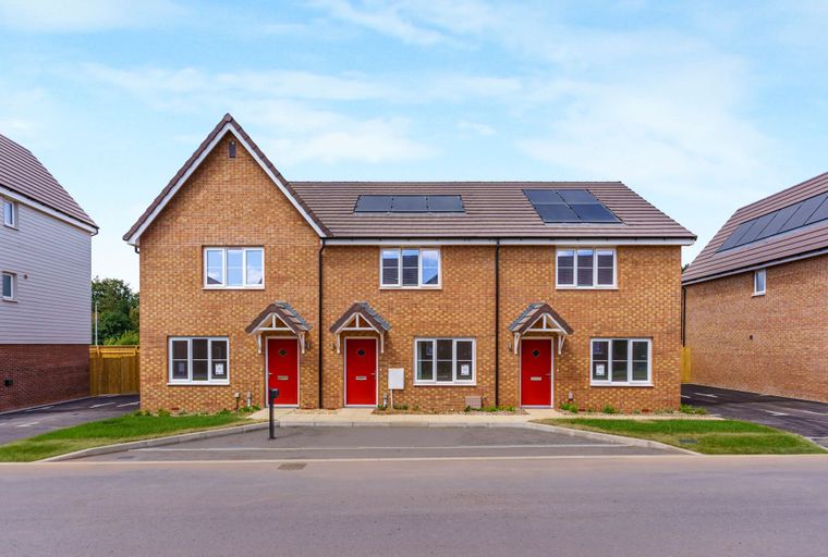 A row of modern brick houses with red doors and solar panels on the roof under a blue sky.