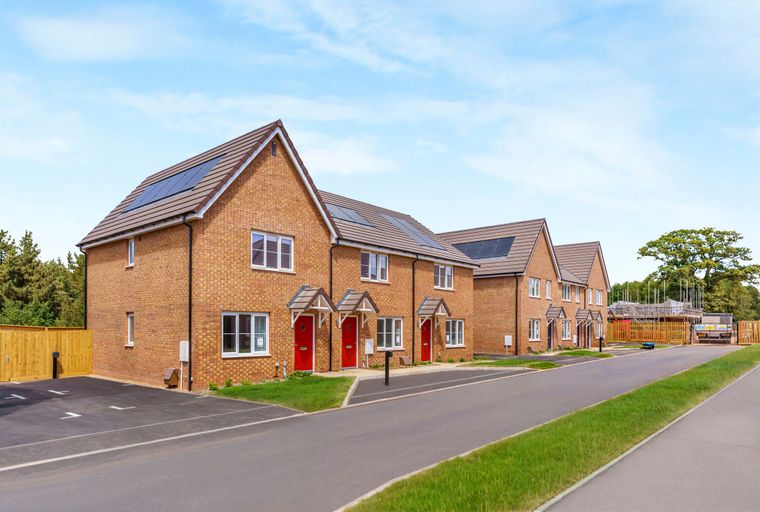 A row of brick townhouses with red front doors and solar panels on the roof.