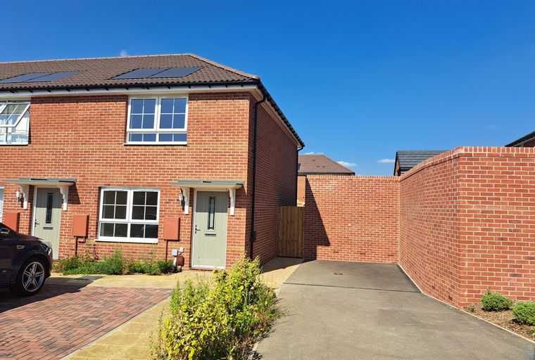 A brick house with white-framed windows and a light grey front door, next to a paved driveway and a brick wall.