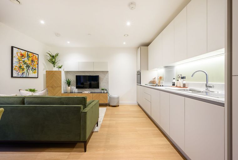 A living room and kitchen area with a green sofa, entertainment unit, and kitchen cabinets.