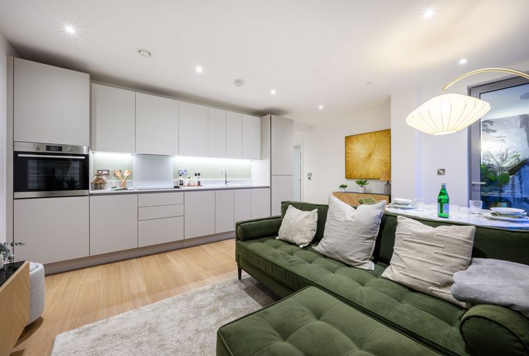 A living room and kitchen area with a green sofa, kitchen cabinets, and a dining table.