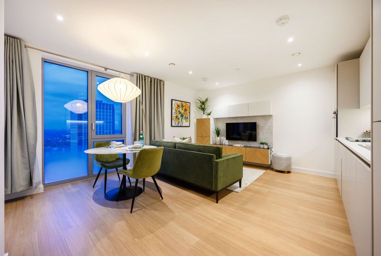 A modern living room and dining area with a green sofa, dining table, and large windows overlooking a city skyline.