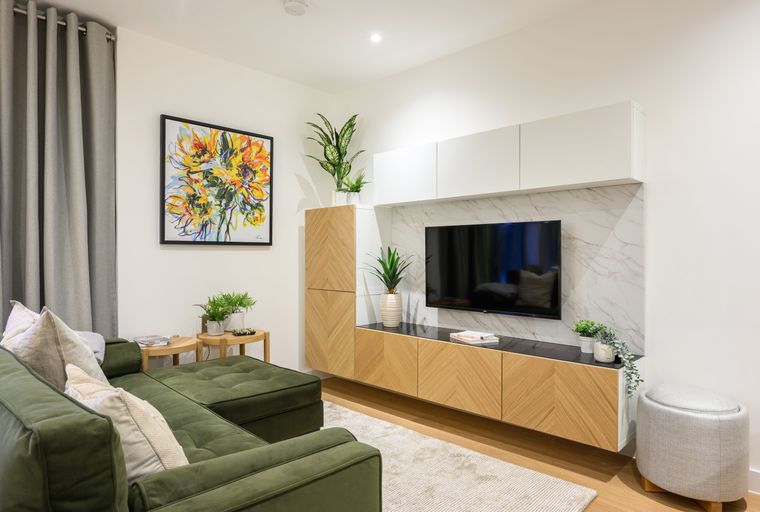 A living room with a green sectional sofa, entertainment unit, and artwork.