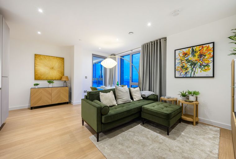 A living room with a green sectional sofa, an arc floor lamp, and artwork on the wall.