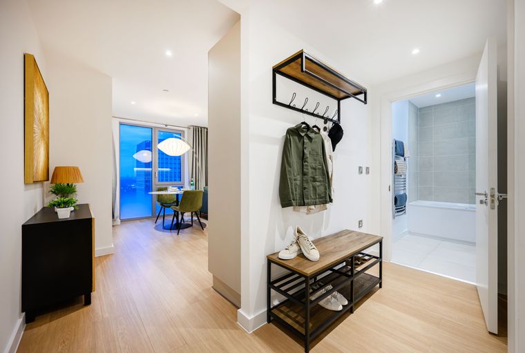 A hallway with a coat rack, bench, shoes, and a doorway to a bathroom.