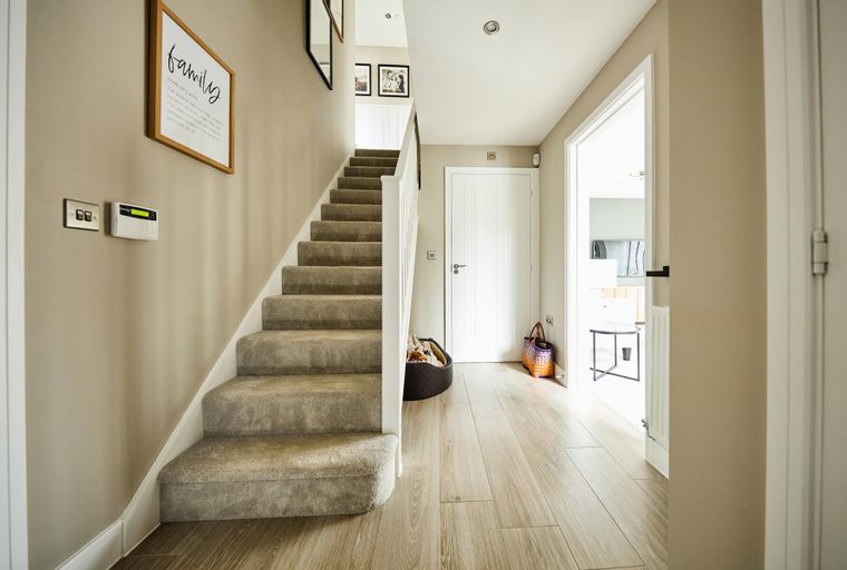 A hallway with a carpeted staircase, wooden flooring, and a white door.