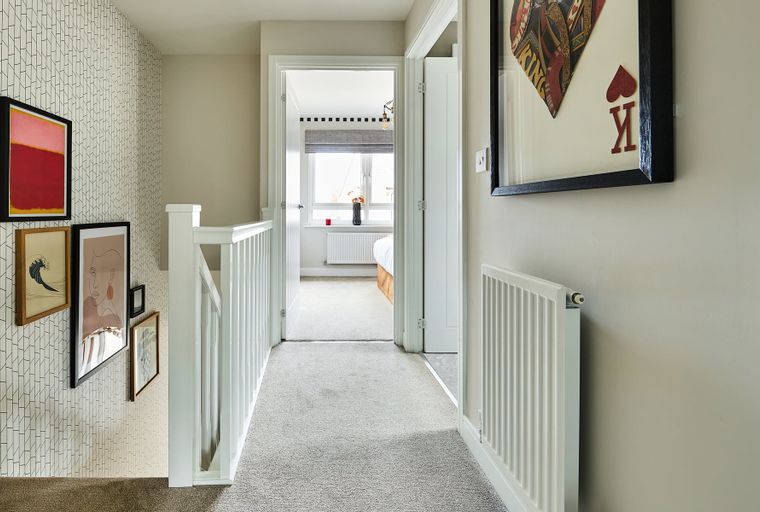 A hallway with a staircase, artwork on the wall, and an open doorway leading to a bedroom.