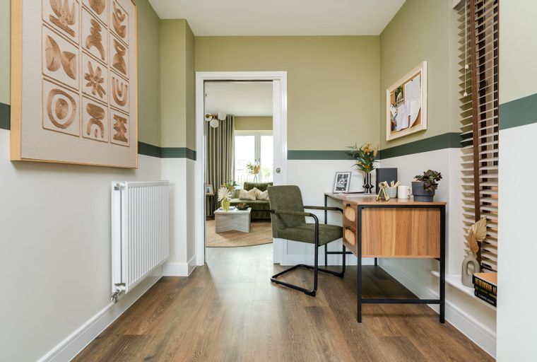 A hallway with a desk, chair, and artwork.