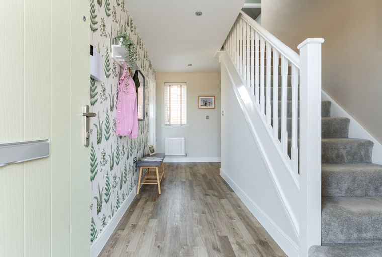A hallway with a front door, patterned wallpaper, a coat rack, a bench, a window, and a staircase.