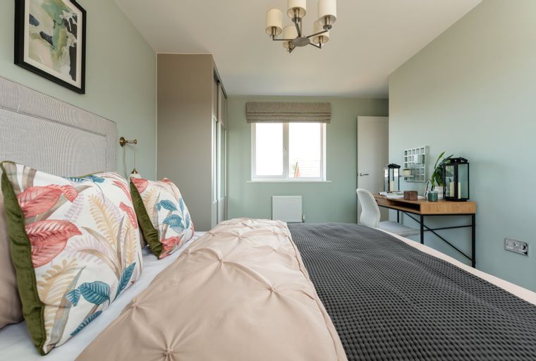 A bedroom with a bed, pillows, a desk, and a window.