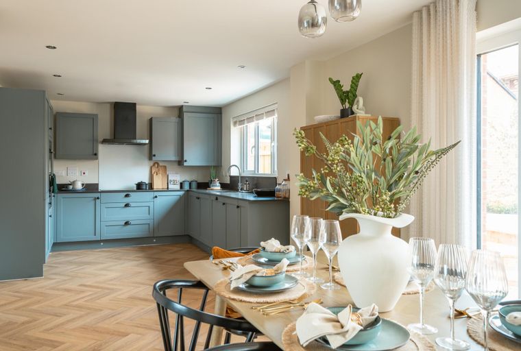 A dining table set for a meal in front of a kitchen with blue cabinets and a herringbone floor.