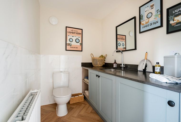 A laundry room with a toilet, sink, cabinets, and decorative wall art.