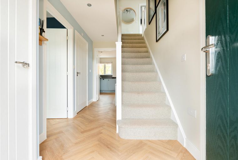 A hallway with a staircase, doors, and a herringbone wood floor.